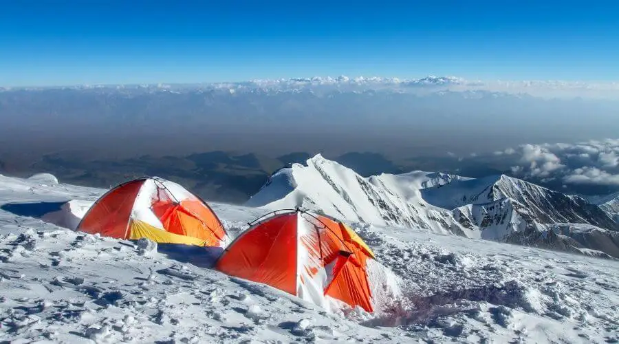 Two orange winter tents pitched in the mountains in heavy snow